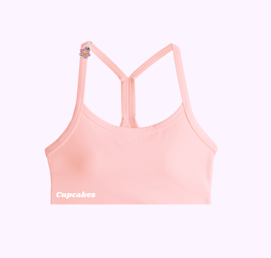 Pink sports bra with 'Cupcakes' text and flower detail on strap.